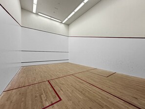 A squash court with wooden flooring and white walls.