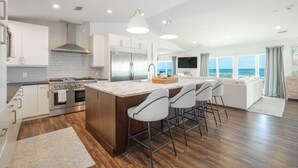 Una cocina moderna con una isla central, electrodomésticos de acero inoxidable y un amplio ventanal con vista al océano.