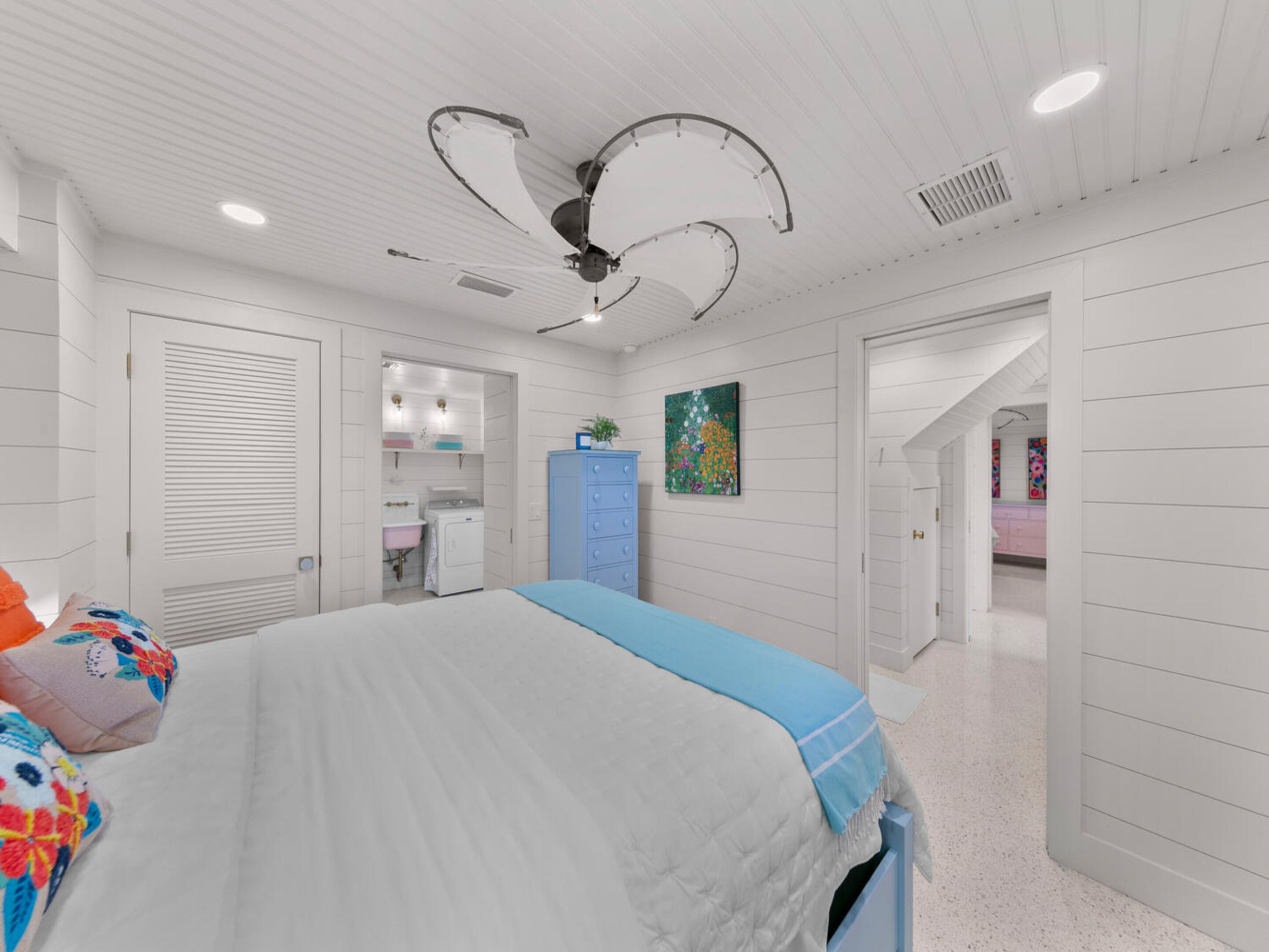A bedroom with a bed, a ceiling fan, a dresser, and a painting on the wall.