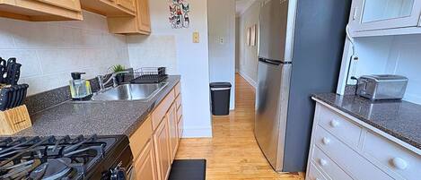 Une cuisine avec des meubles de rangement en bois, une cuisinière à gaz, un réfrigérateur et une poubelle.