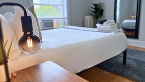 A neatly made bed with white linens, a bedside lamp, and a small plant on the nightstand. - Charming 1BR Apt in Evanston (Evanston)