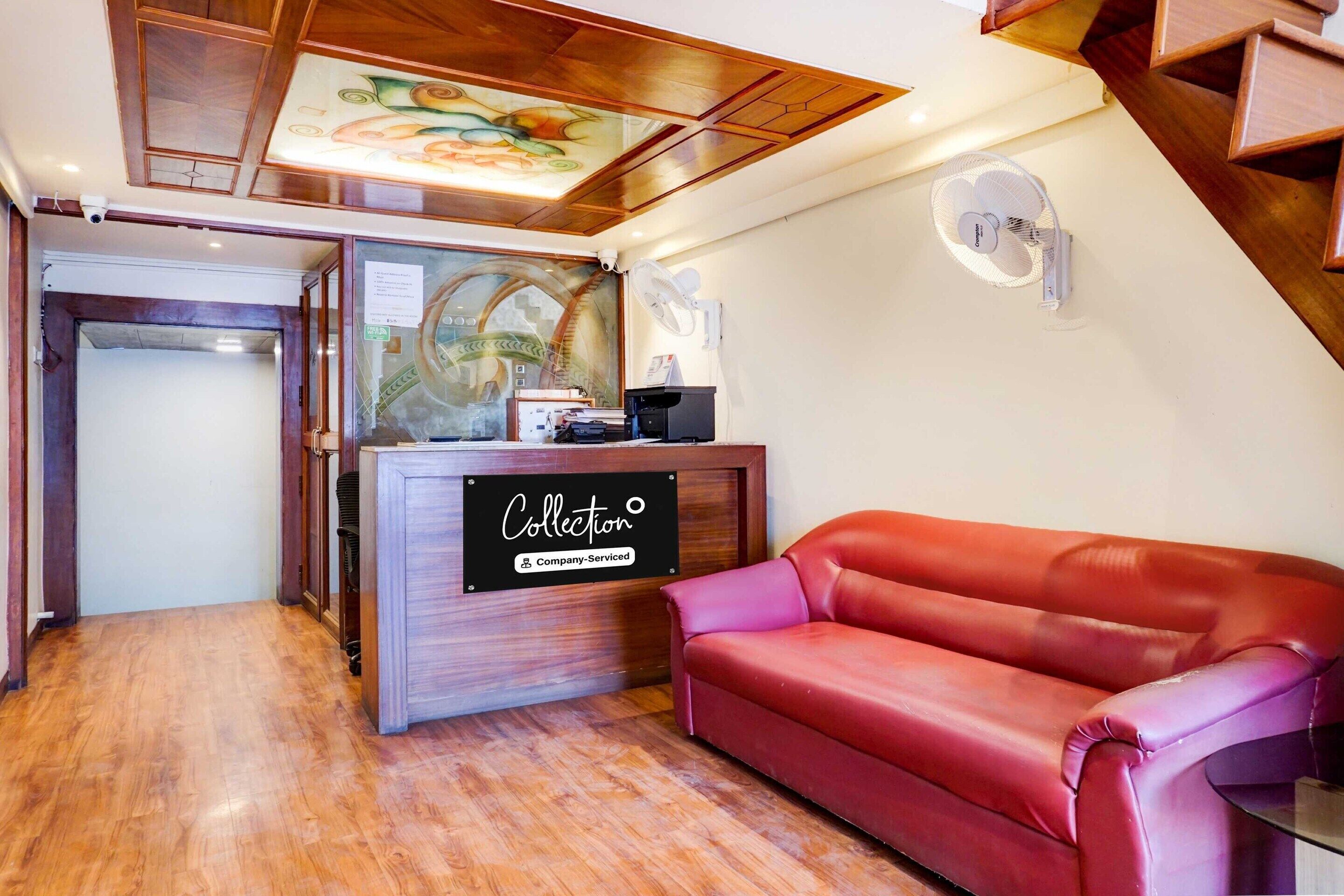 A reception area with a wooden desk, a red leather couch, and a ceiling with a decorative design.