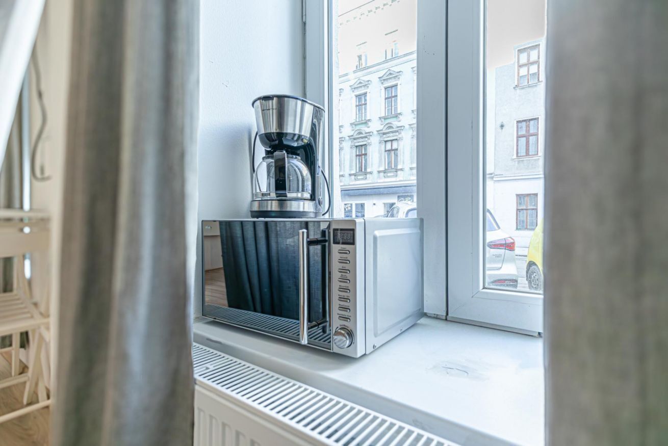 Eine Mikrowelle und eine Kaffeemaschine stehen auf einem Fensterbrett mit Blick auf Gebäude und ein Auto vor dem Haus.