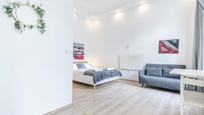 A modern bedroom with a bed, a gray sofa, a white desk, and two paintings on the wall.
