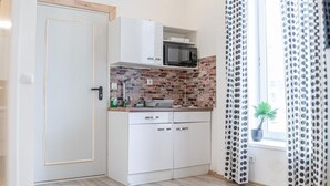 A compact kitchen with white cabinets, a microwave, and a brick backsplash.