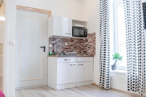 Cozinha compacta com armários brancos, micro-ondas e painel de tijolos.