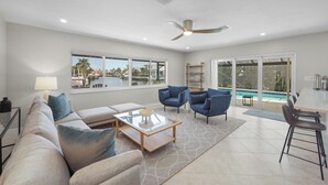 A spacious living room with a large window, a ceiling fan, and a view of a pool and palm trees. - Canal home w/ pool, kayak, foosball, and ping pong (Marco Island)