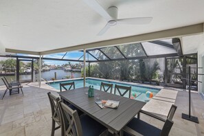 A covered outdoor area with a pool, seating, and a view of the water. - Canal home w/ pool, kayak, foosball, and ping pong (Marco Island)