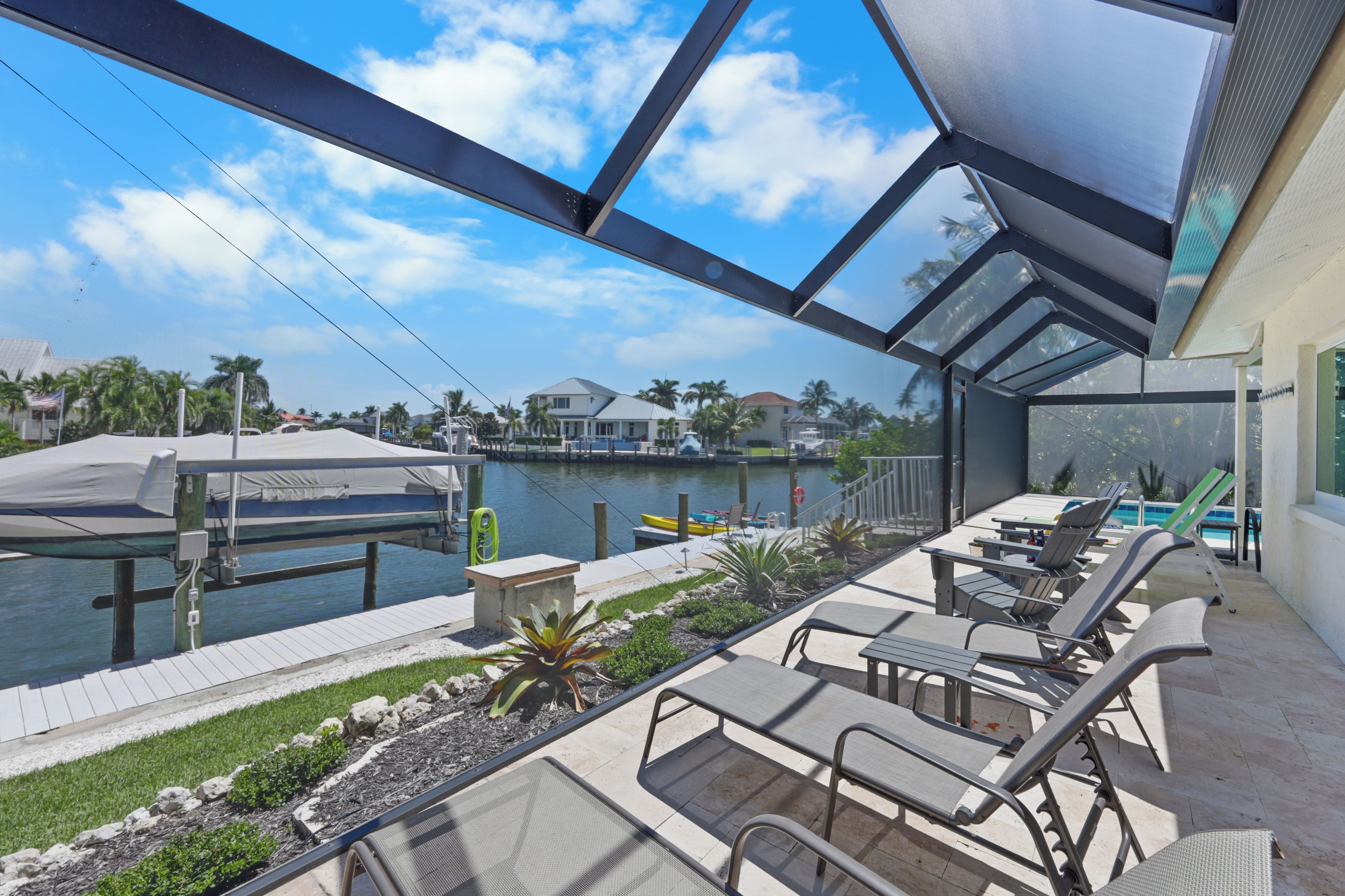 Een overdekt buitengebied met lounge fauteuils en uitzicht op een wateroppervlak en huizen op de achtergrond.