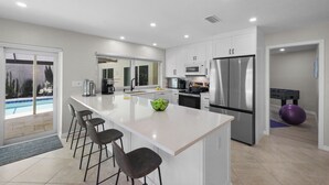 A modern kitchen with a large island, bar stools, stainless steel appliances, and a view of a pool. - Canal home w/ pool, kayak, foosball, and ping pong (Marco Island)