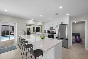 A modern kitchen with a large island, bar stools, stainless steel appliances, and a view of a pool. - Canal home w/ pool, kayak, foosball, and ping pong (Marco Island)