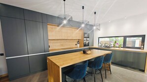 Una cocina moderna con isla de madera, armarios oscuros e iluminación colgante.