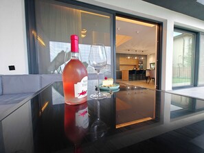 A modern living room with a glass table, a bottle of rosé wine, and a glass.