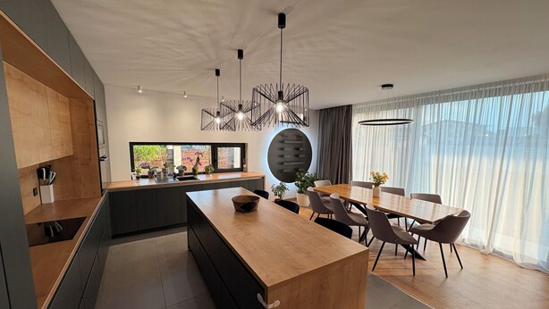 Una cocina moderna con una isla central, muebles oscuros y un comedor con mesa y sillas de madera.