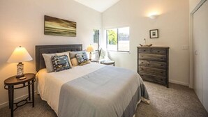 A bedroom with a bed, bedside tables, a dresser, a window, and a painting on the wall.