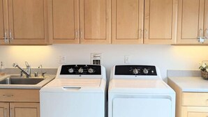 A laundry room with two white washing machines, wooden cabinets, a sink, and a countertop.