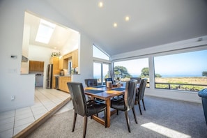 A modern kitchen with a dining area, large windows, and a view of the outdoors.