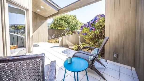 A patio area with wicker furniture, a blue table, and a view of the garden.