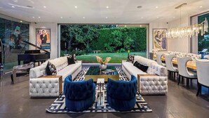 A modern living room with a grand piano, plush seating, and a view of a lush garden. - Alta Royale - Exquisite Designer Retreat Near Soho House & Rodeo Drive (West Hollywood)
