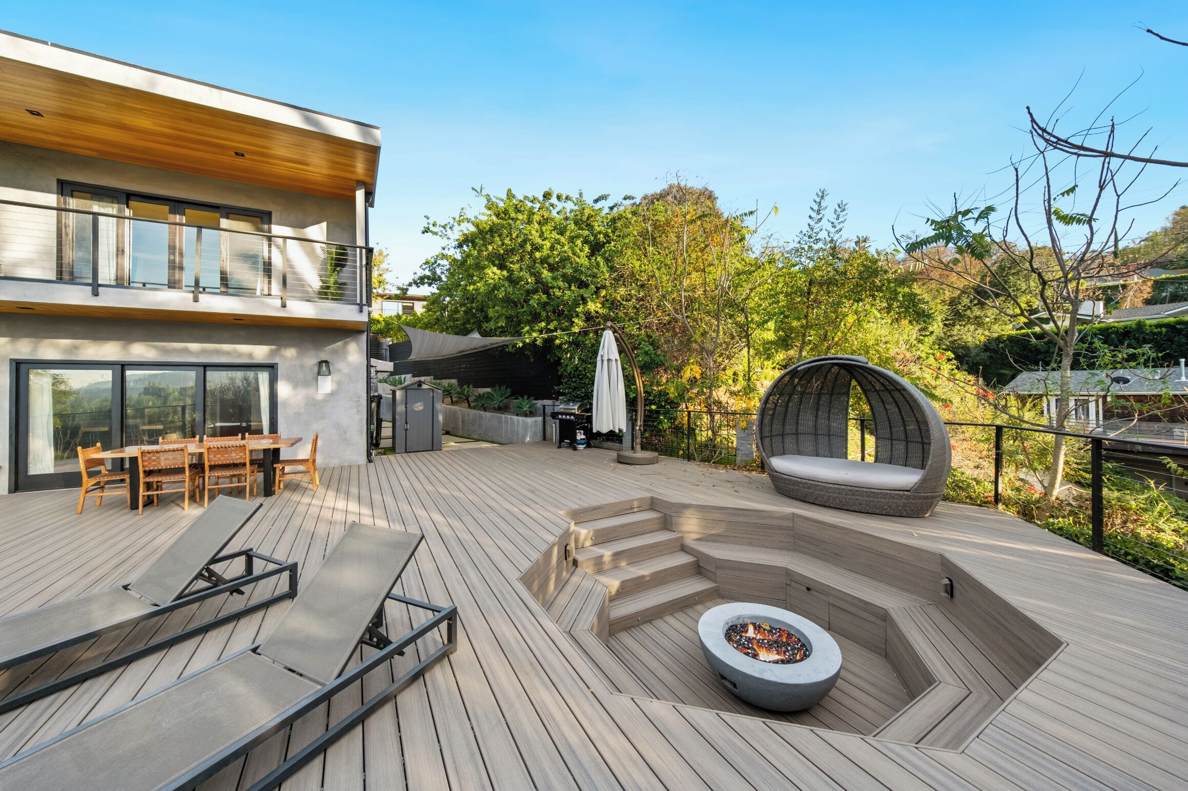 A modern outdoor deck with a fire pit, seating area, and a dining setup.