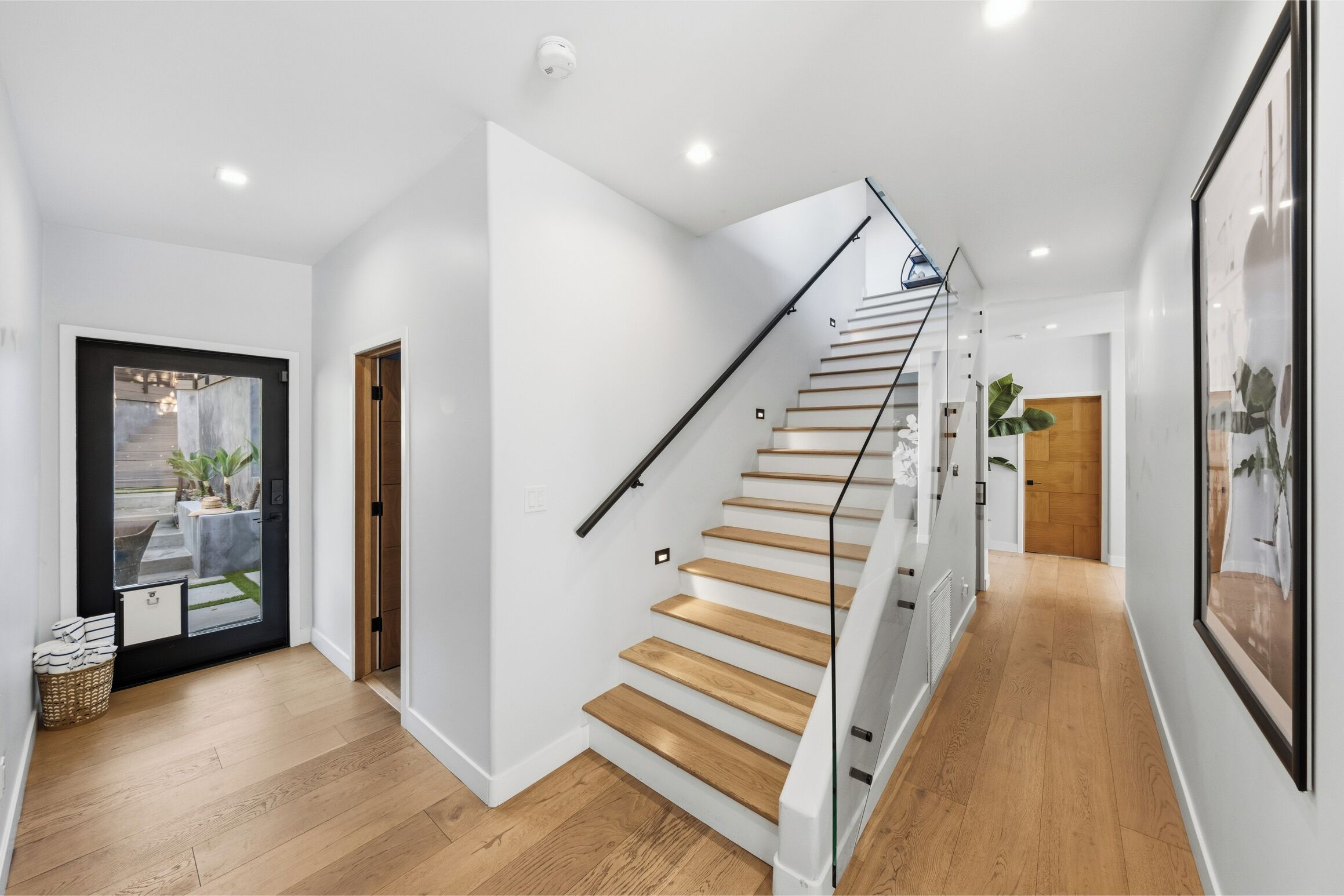 Een modern interieur met een houten trap, witte muren en een glazen deur naar een buitenruimte.