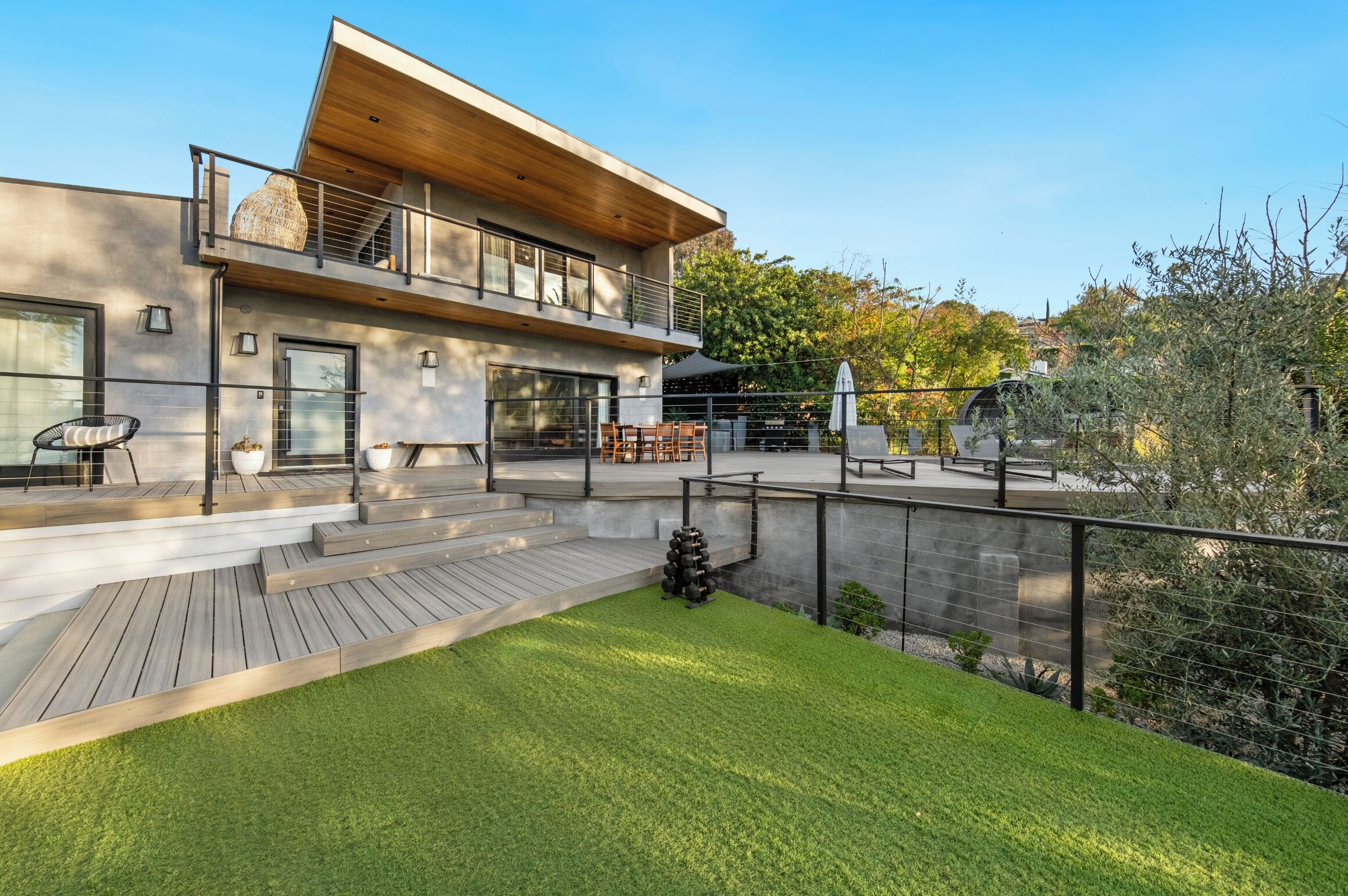 A modern two-story house with a wooden deck, outdoor seating, and a well-maintained lawn.