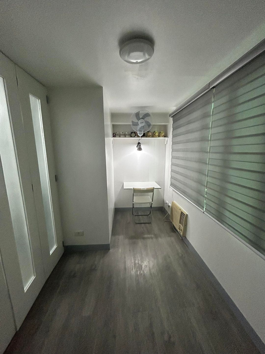 Een smalle gang met een witte wastafel, een ventilator en een radiator.