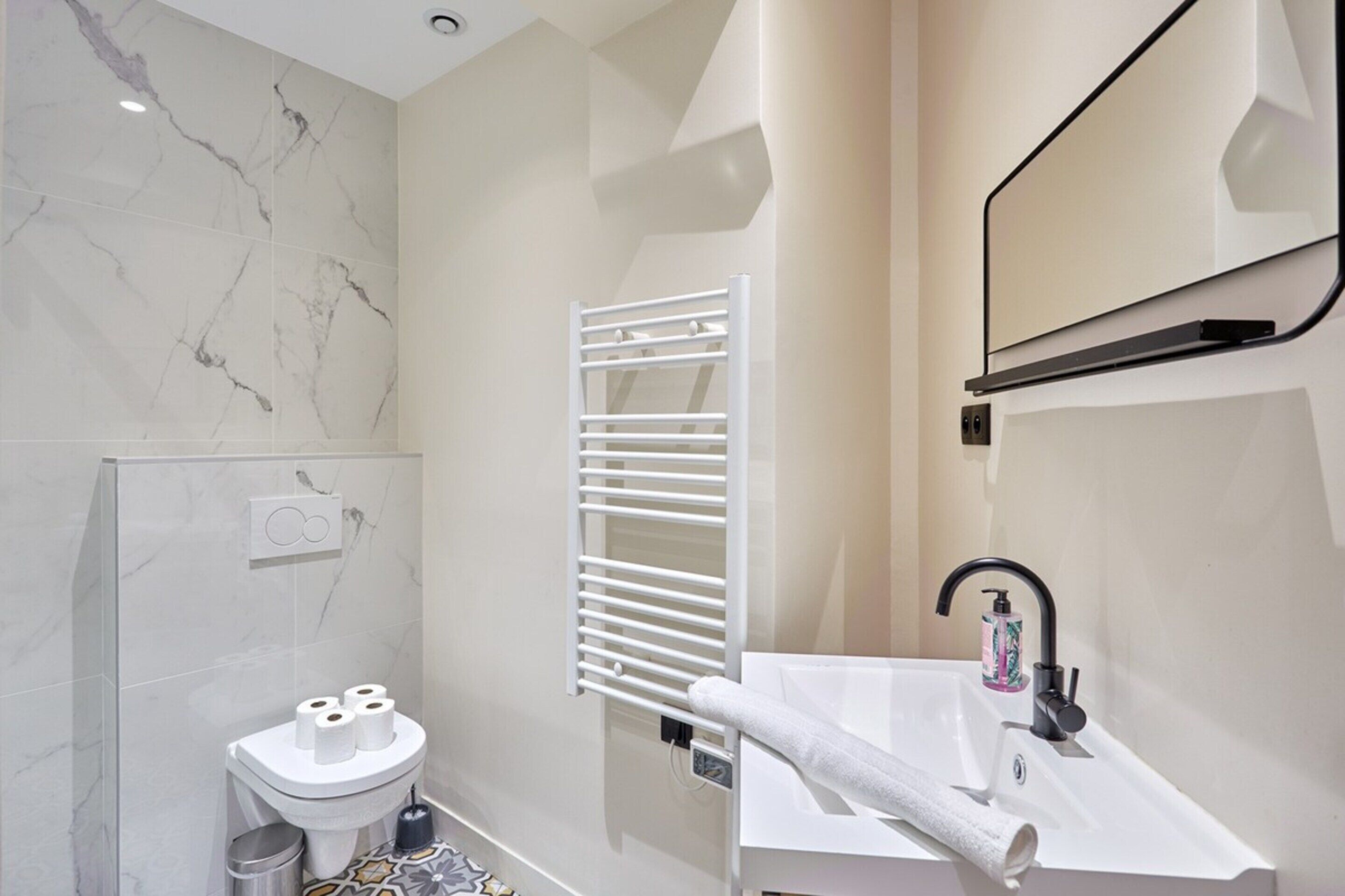 A modern bathroom with a toilet, sink, towel rack, and a mirror.