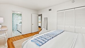 Une chambre à coucher avec un lit, une table de chevet, une commode et une salle de bain visible à travers une porte ouverte.
