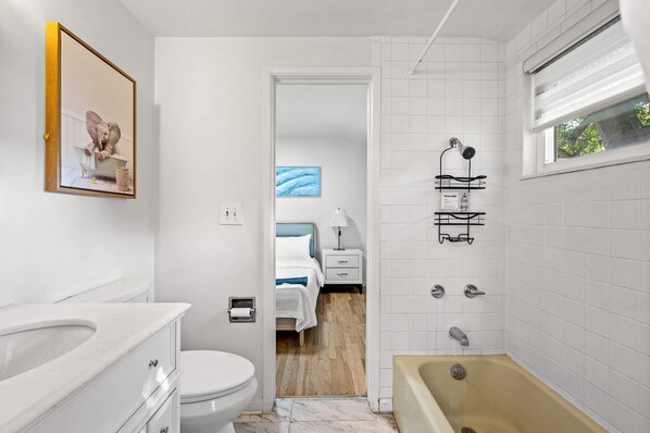 A modern bathroom with a bathtub, toilet, and sink. There is a framed picture on the wall and a window with a view of trees. - Perfect Family Home With Fireplace Spacious Yard (Duarte)