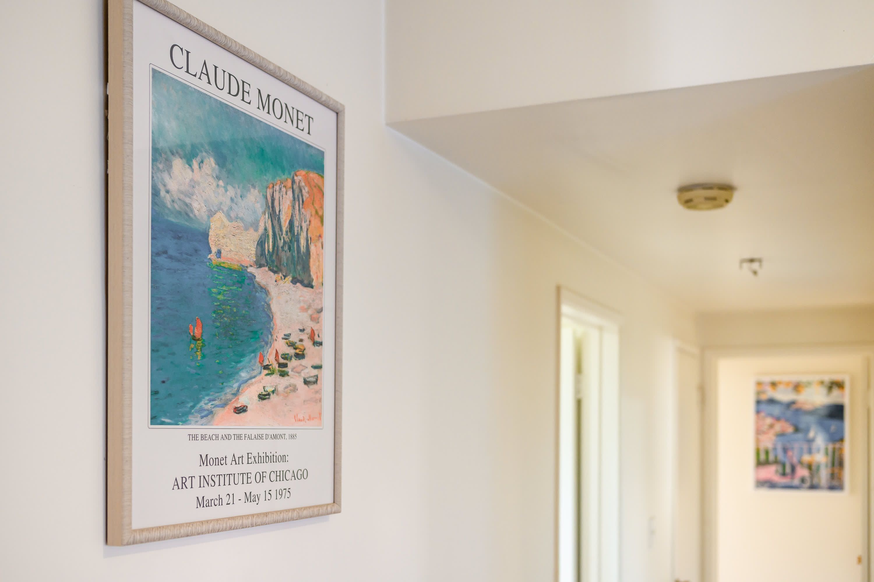 A framed artwork of Claude Monet's 'The Beach and the Palace of Versailles' from 1885, displayed on a wall in a hallway.