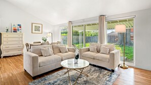 Un salon spacieux avec deux canapés beige, une table basse ronde et une grande fenêtre donnant sur un jardin.