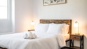 A neatly made bed with white linens and rolled towels, two bedside lamps, and a framed picture on the wall. - Bright Airy 5B Home Workspace Outdoor Lounge (Moreno Valley)