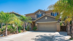 A two-story residential house with a garage, surrounded by mature trees and a well-maintained lawn. - Bright Airy 5B Home Workspace Outdoor Lounge (Moreno Valley)
