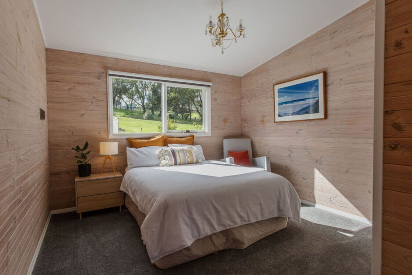 Une chambre à coucher comprenant un lit, une table de chevet, une lampe et une fenêtre donnant sur un paysage verdoyant.