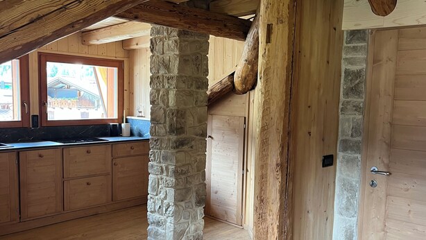 Un interior rústico de madera con vigas a la vista, un pilar de piedra y una puerta de madera.
