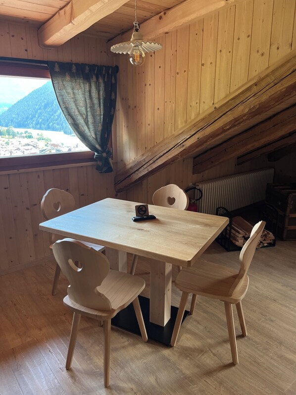 A wooden dining room with a table and chairs, a hanging light fixture, and a view of a mountainous landscape through a window.