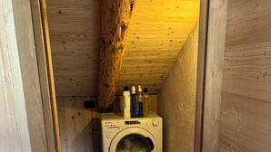 Un lavadero pequeño con lavadora, paredes de madera y techo inclinado.