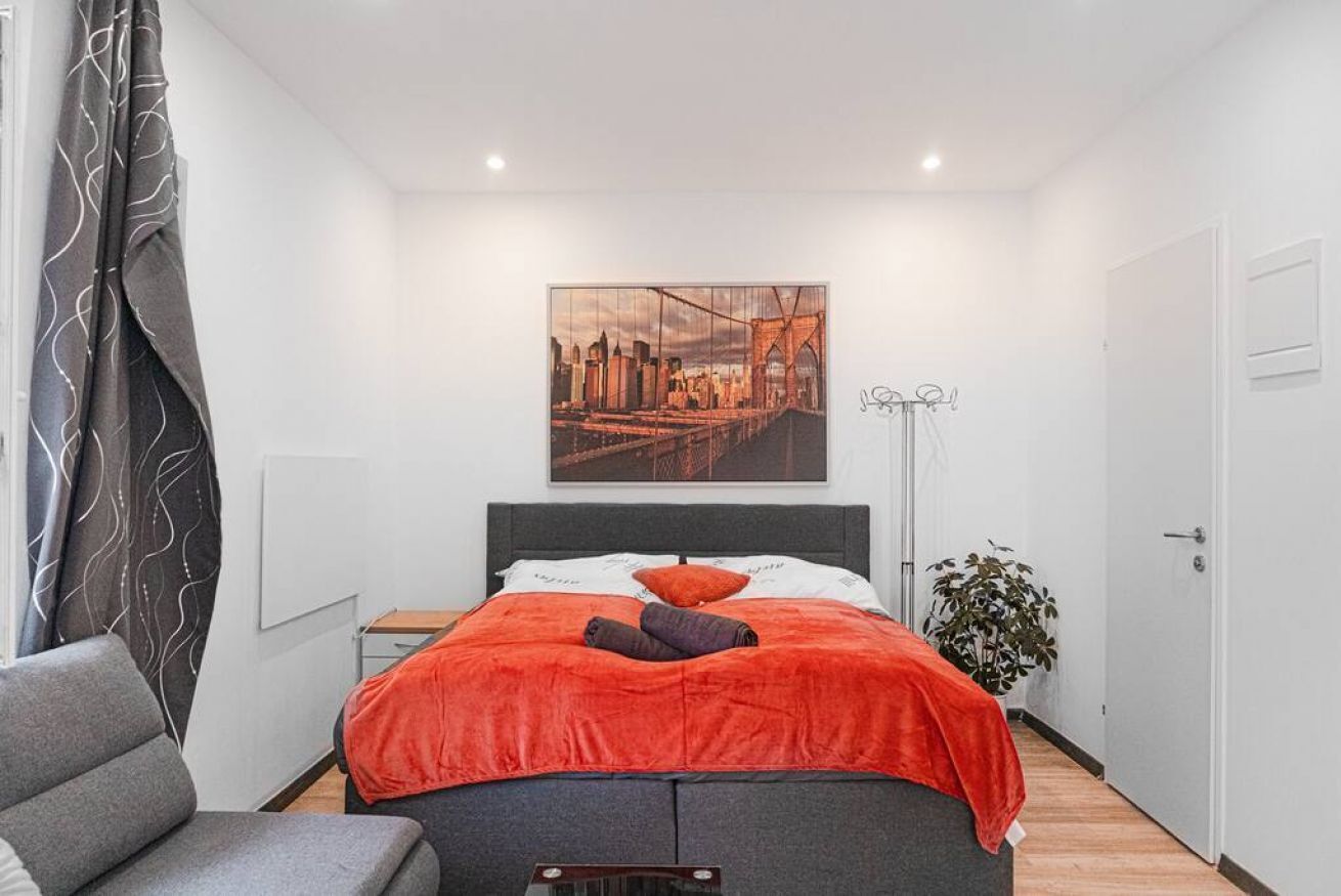 Une chambre à coucher avec un lit, une chaise, une plante et un tableau représentant un paysage urbain accroché au mur.