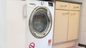 A front-loading washing machine in a kitchen with a countertop and cabinets.
