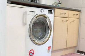 A front-loading washing machine in a kitchen with a countertop and cabinets.