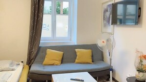 A room with a sofa, a bed, a TV, and a fan.