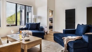 A modern living room with two dark blue sofas, a wooden coffee table, and a large window offering a view of greenery. - Cozy Luxe Home,Breathtaking Mtn. Views of fall foliage, Outdoor sauna,large deck (Sevierville)