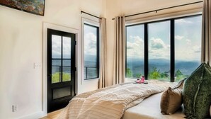 A bedroom with a large window, a bed with a striped blanket, and a view of the landscape. - Cozy Luxe Home,Breathtaking Mtn. Views of fall foliage, Outdoor sauna,large deck (Sevierville)