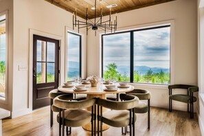 A dining area with a round table, six chairs, and a view of mountains through large windows.