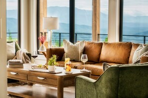 A modern living room with a leather sofa, a wooden coffee table, and a view of mountains through large windows.