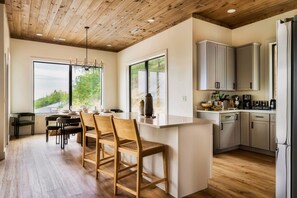 A modern kitchen with wooden flooring, a dining area with chairs, and a view through large windows.
