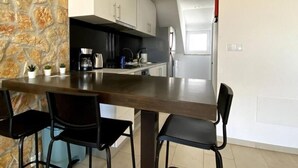 A modern kitchen with a stone accent wall, a wooden dining table, and black chairs. - Casa do Rio, Algarve, charming renovated traditional house, ideal location (Parchal)