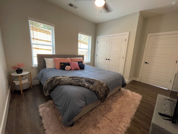 A bedroom with a bed, two windows, a wardrobe, and a small table with a vase.