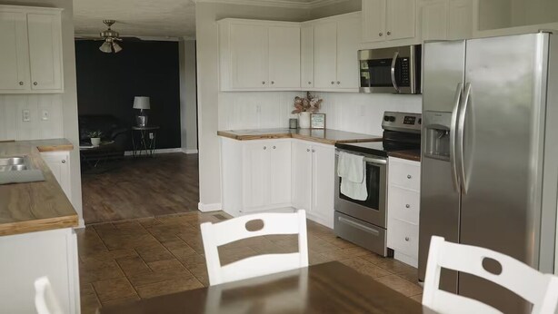 Cozinha moderna com armários brancos, eletrodomésticos de aço inoxidável e uma mesa de jantar de madeira.